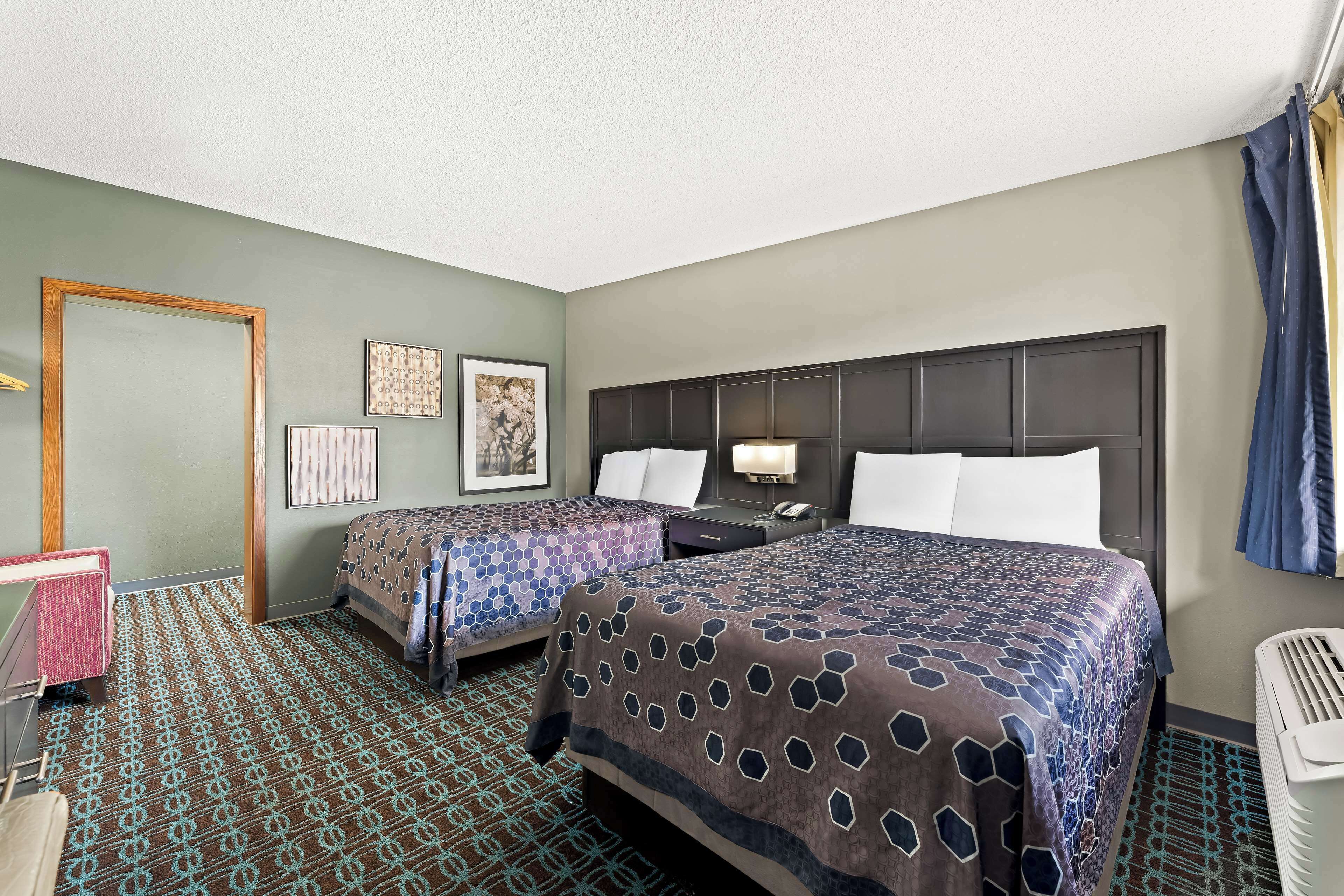 A hotel room with two beds, a desk, a chair, a trash bin, and a door.