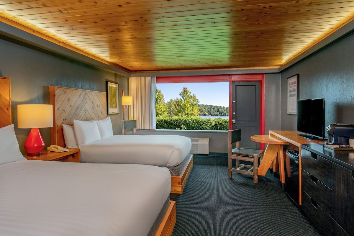 A hotel room with two beds, a desk, a TV, and a view of a lake.