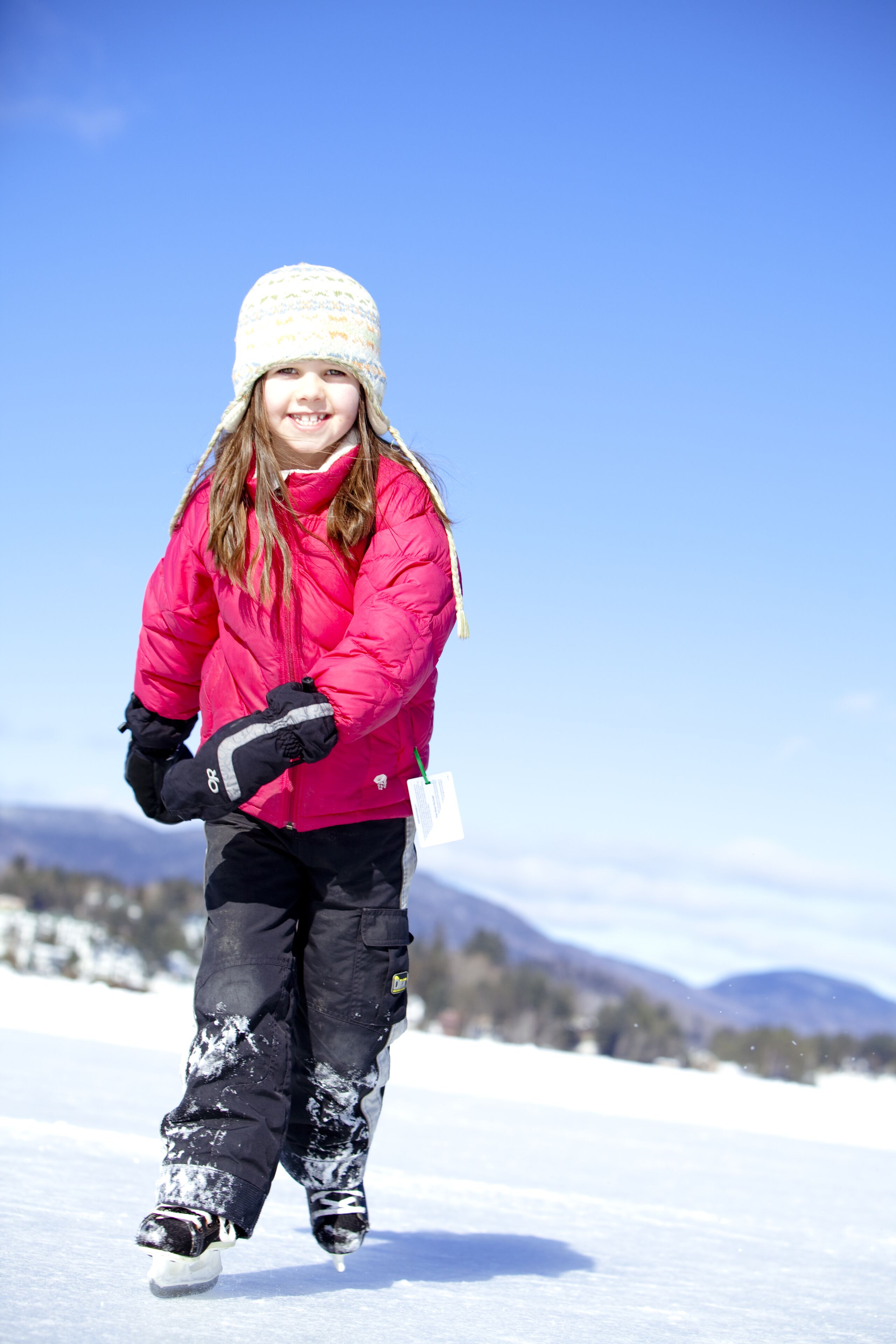 A person in winter clothing standing on snow-covered ground with mountains in the background.