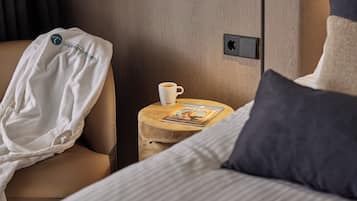 Una habitación de hotel con una cama, una mesita de noche de madera con una revista, una bata blanca y una taza de café.