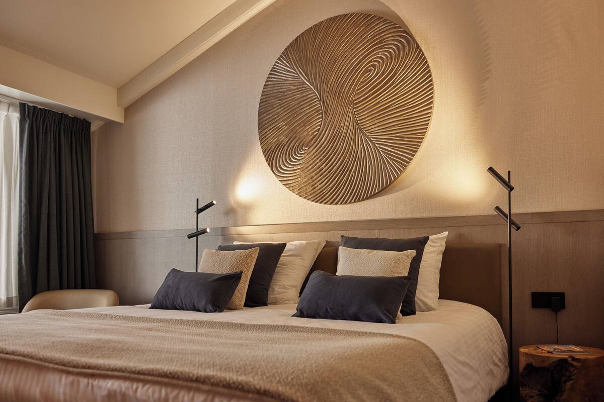 Une chambre d’hôtel moderne avec un grand lit, une œuvre d’art murale de forme circulaire et une table de chevet avec une lampe.