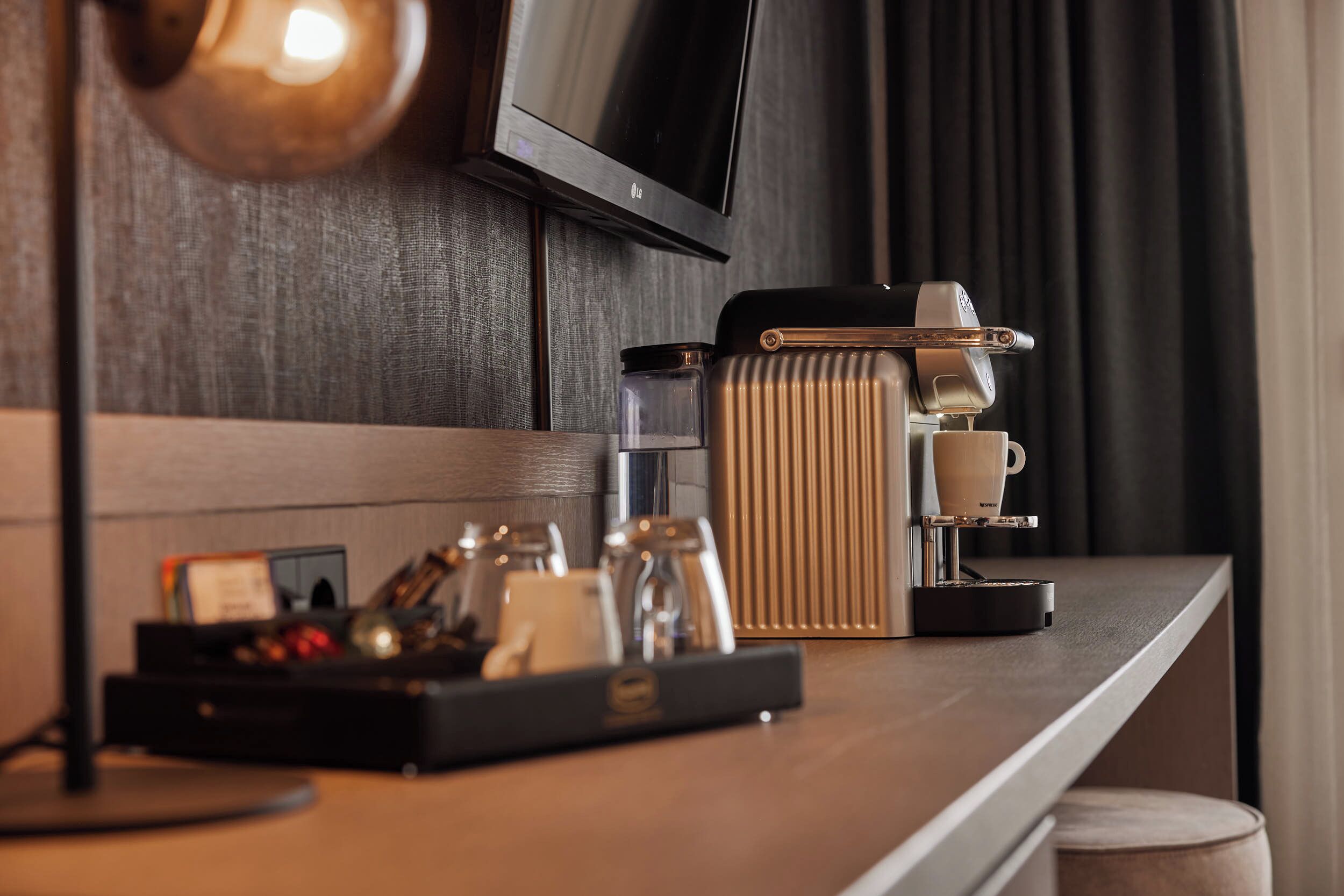 Ett modernt hotellrum med en träbeklädd disk, en kaffemaskin, en kopp och ett bricka med diverse tillbehör.