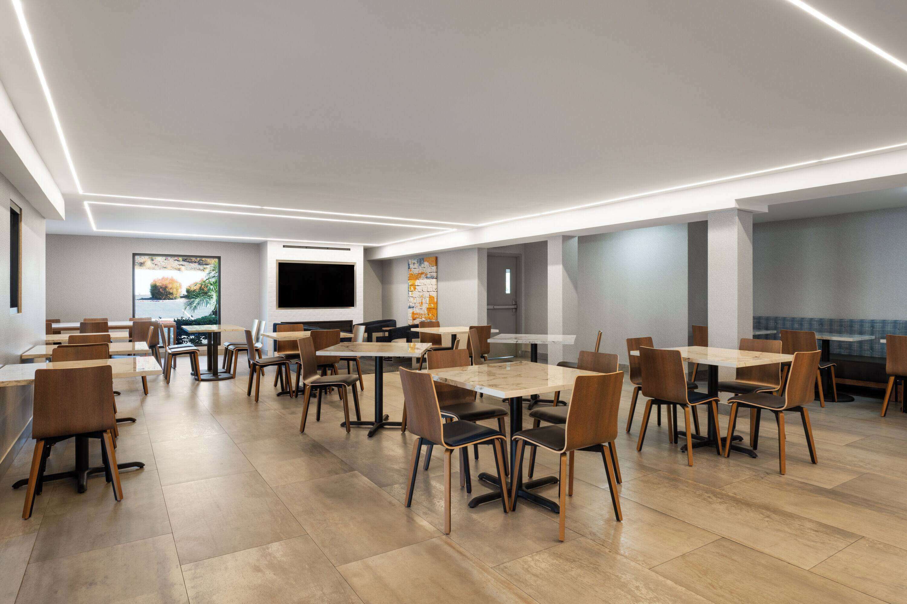 Un espace de restauration moderne doté de plusieurs tables et chaises, d’une grande fenêtre offrant une vue agréable et d’un design contemporain au niveau du plafond.