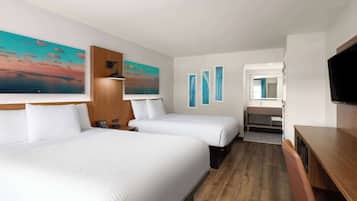 A hotel room with two beds, a wooden desk, a TV, and artwork on the walls.