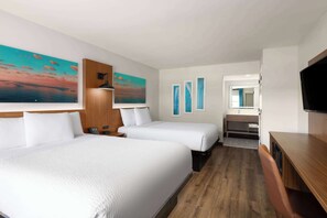 A hotel room with two beds, a wooden desk, a TV, and artwork on the walls.