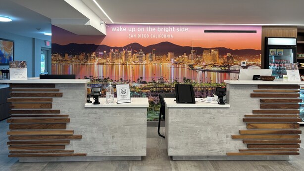Zona de recepción de un hotel con un mural de la ciudad, un cartel de 'No Fumar' y un refrigerador lleno de bebidas.