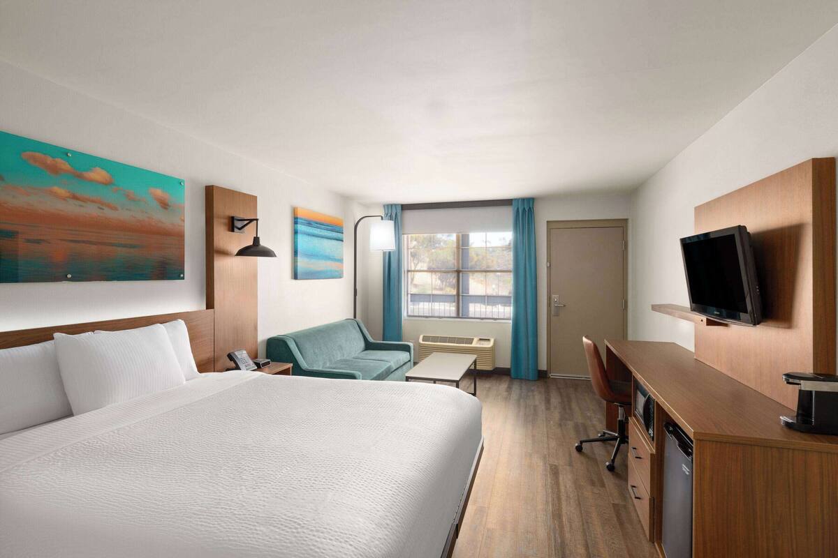 Une chambre d’hôtel équipée d’un lit, d’un bureau, d’une chaise, d’une télévision et d’une fenêtre avec des rideaux.