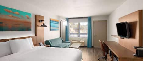 Habitación de hotel con cama, escritorio, silla, televisor y ventana con cortinas.