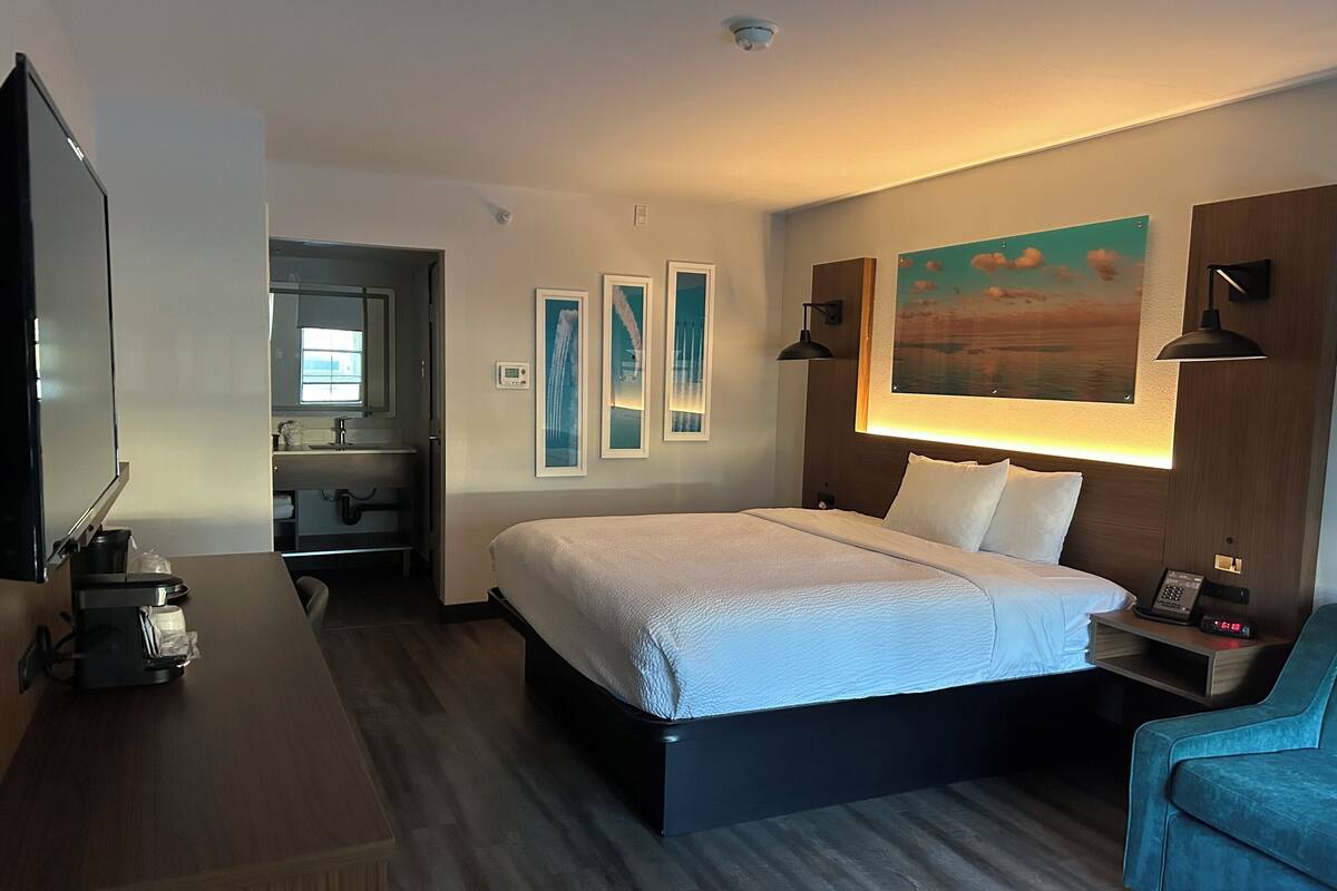 Une chambre d’hôtel comprenant un lit, un bureau, une chaise, une télévision, une salle de bain et des œuvres d’art accrochées aux murs.