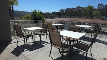 Un patio al aire libre con mesas y sillas, barandilla blanca y vistas a un paisaje montañoso.