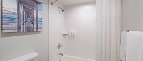 A bathroom with a toilet, bathtub, shower, and a painting of a pier.