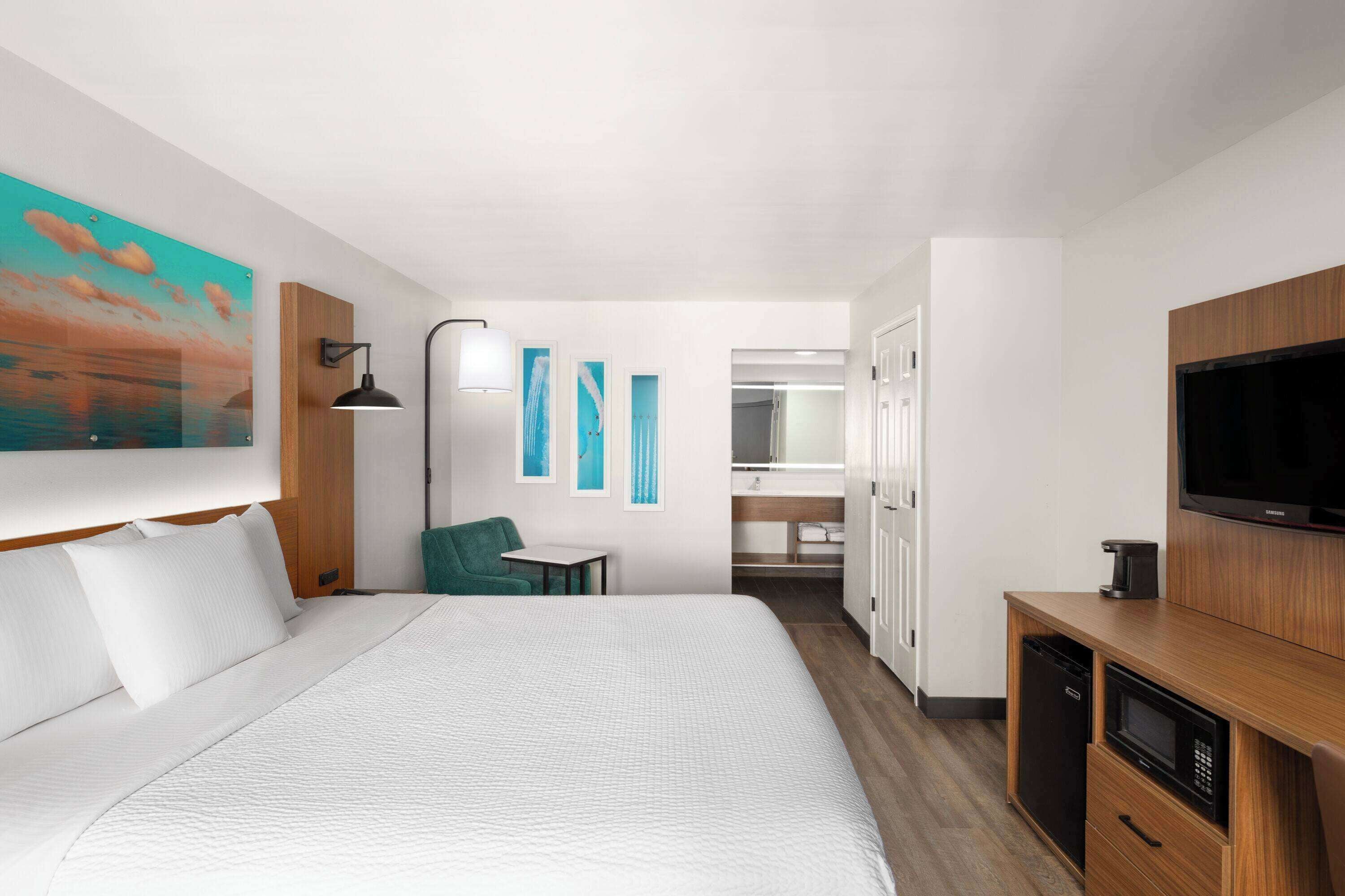 A hotel room with a bed, a desk, a television, and a bathroom visible through an open door.