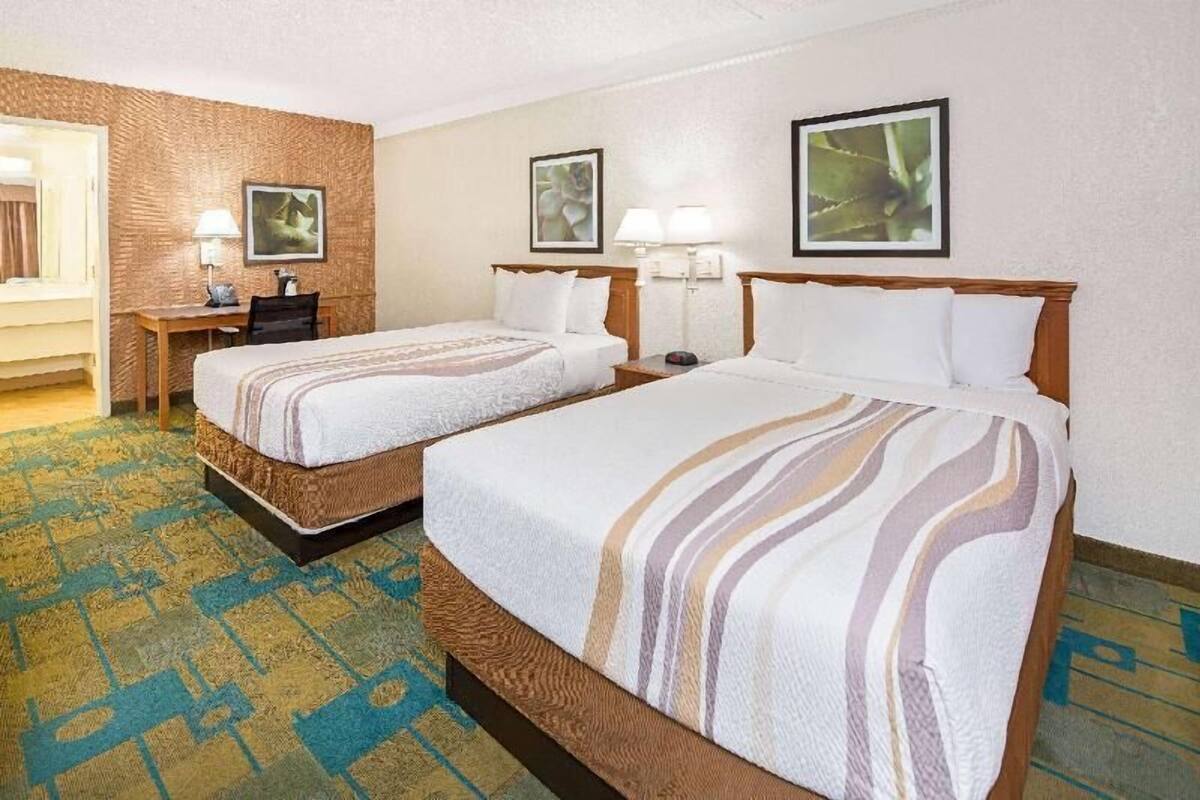 Une chambre d’hôtel avec deux lits, un bureau, une chaise et une moquette à motifs.