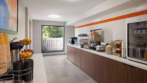 Un área de cocina moderna con estación de café, frutero y refrigerador de vidrio que exhibe alimentos.