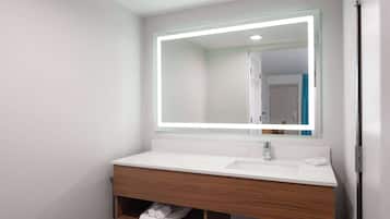 Un baño moderno con lavamanos blanco, tocador de madera y espejo con marco iluminado.