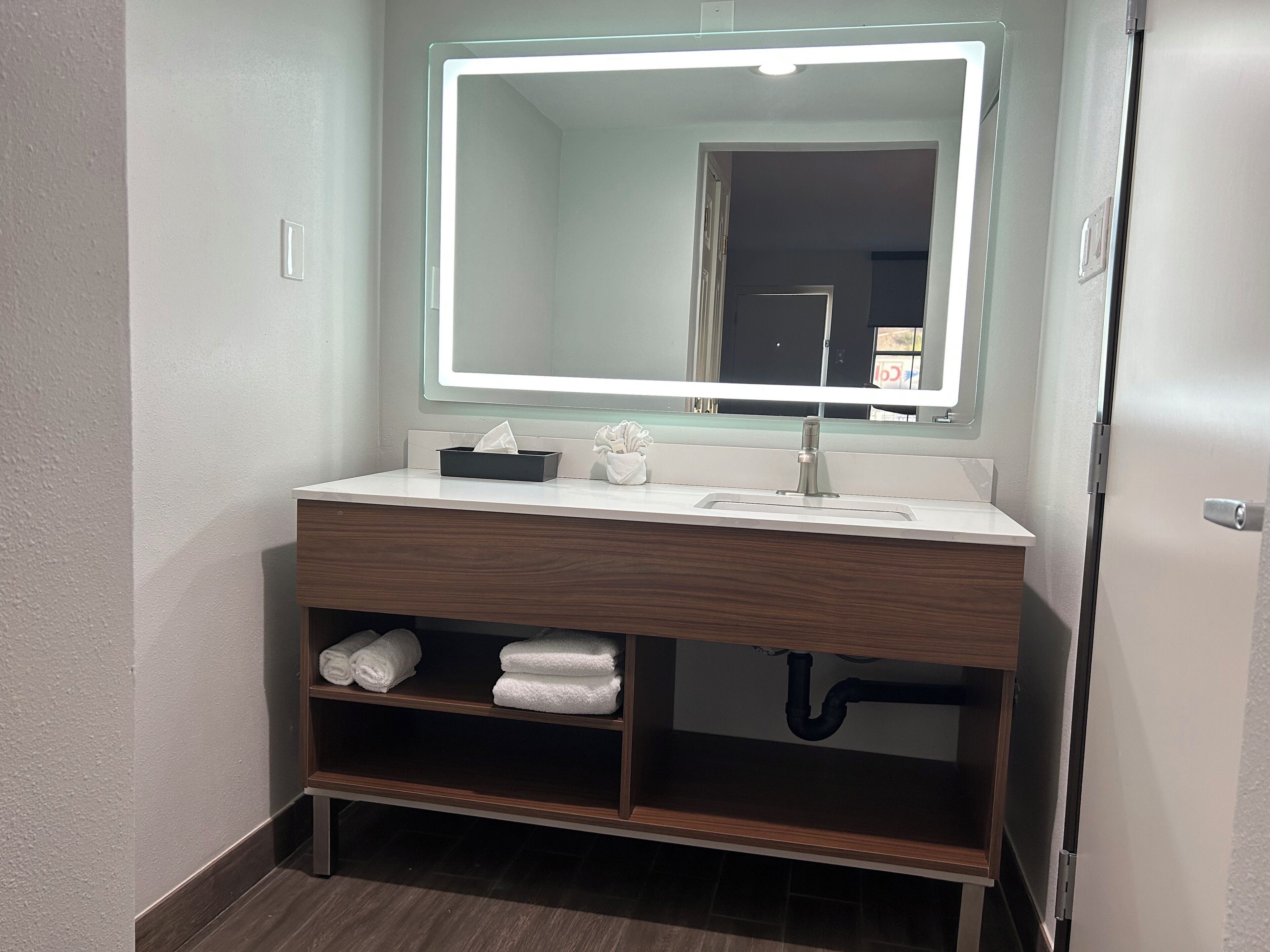 Un baño con lavamanos blanco, espejo con luz y toallero.