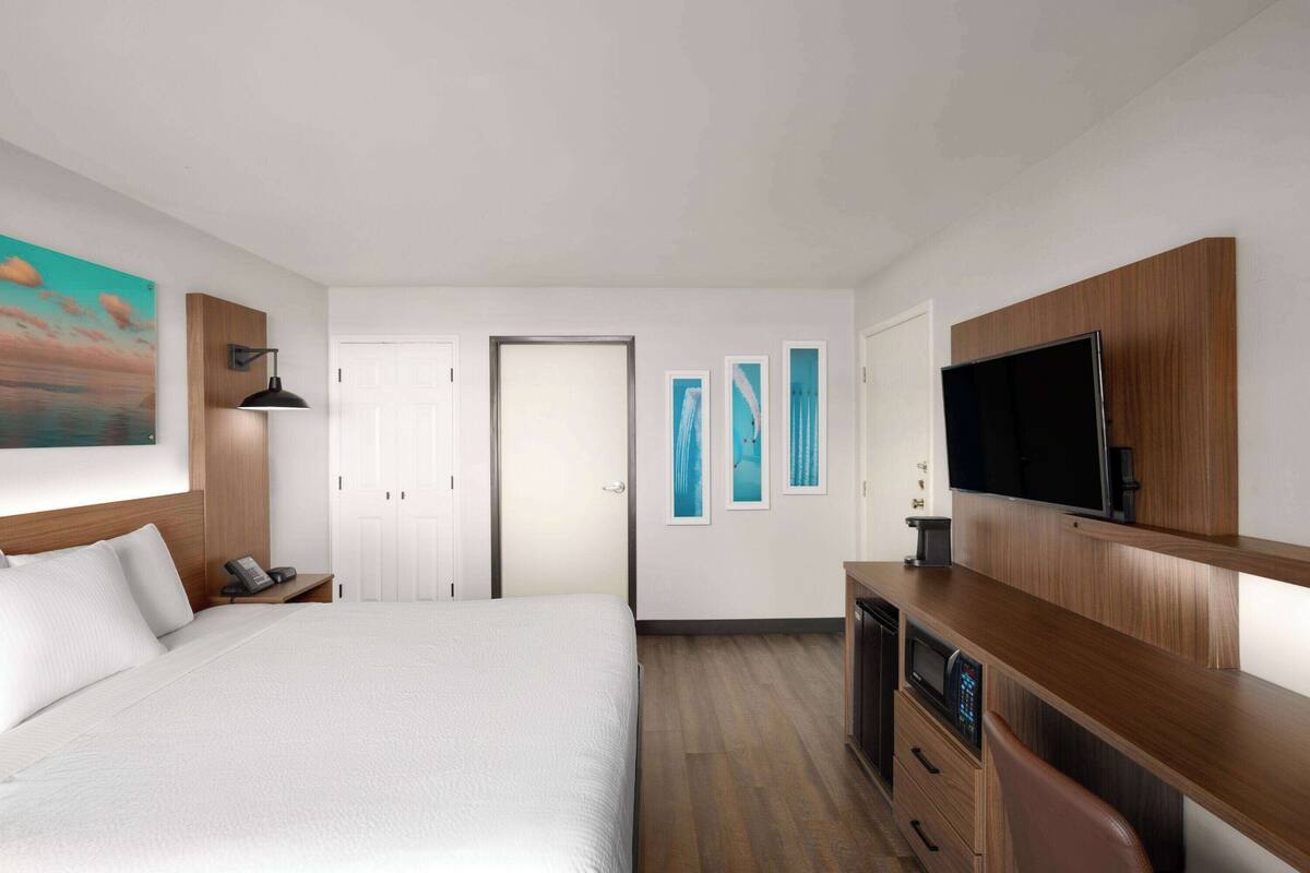 Une chambre d’hôtel dotée d’un grand lit, d’un bureau avec un téléviseur à écran plat, d’une armoire en bois et d’œuvres d’art accrochées aux murs.