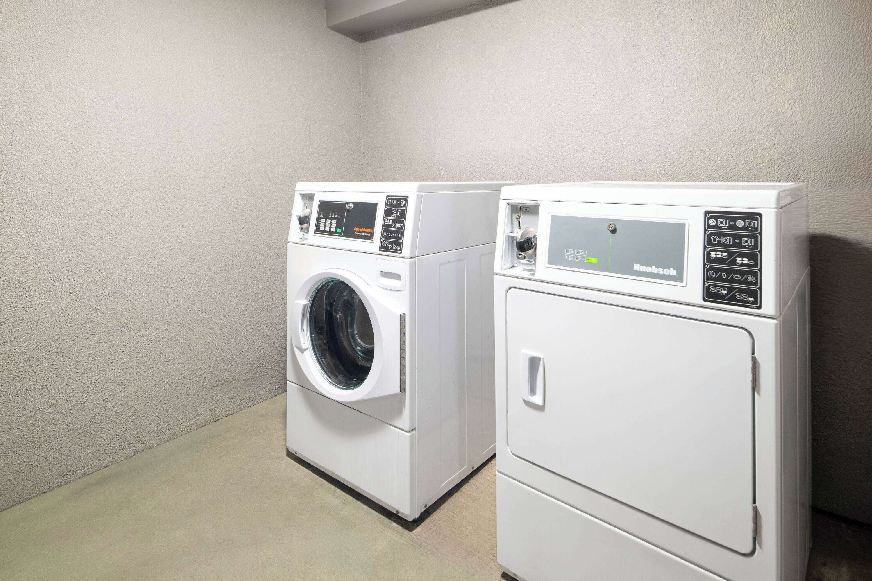 Two white front-loading washing machines in a laundry room with a plain wall and a concrete floor.