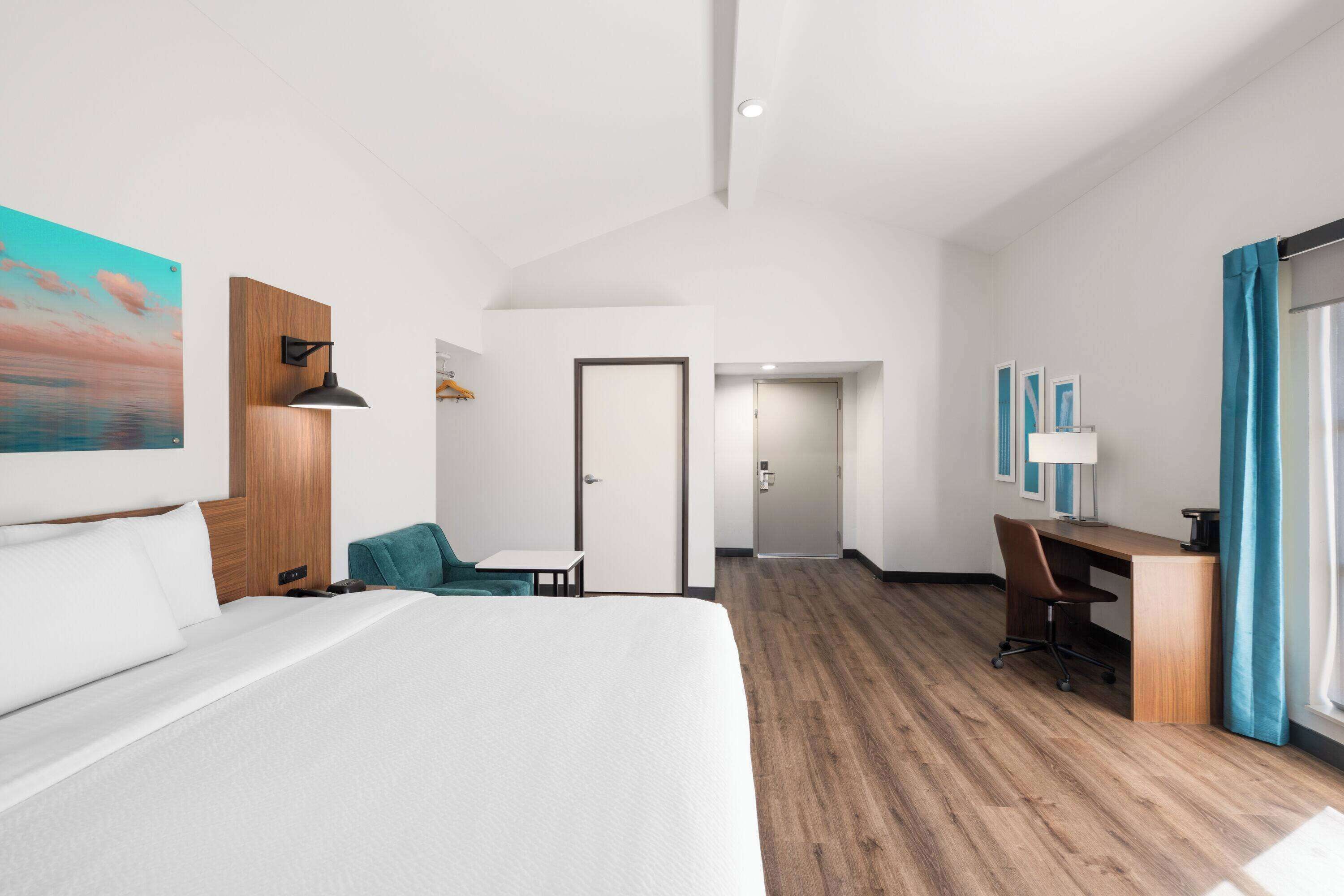 Ein modernes Hotelzimmer mit einem großen Bett, einem Schreibtisch, einem Stuhl und Blick auf den Flur.