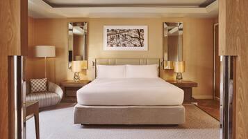 Habitación de hotel con una cama grande, dos mesitas de noche con lámparas, un sofá, un cuadro enmarcado en la pared y un espejo.