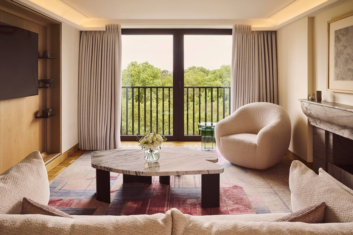 A living room with a round coffee table, a sofa, a chair, a fireplace, and a balcony with curtains.