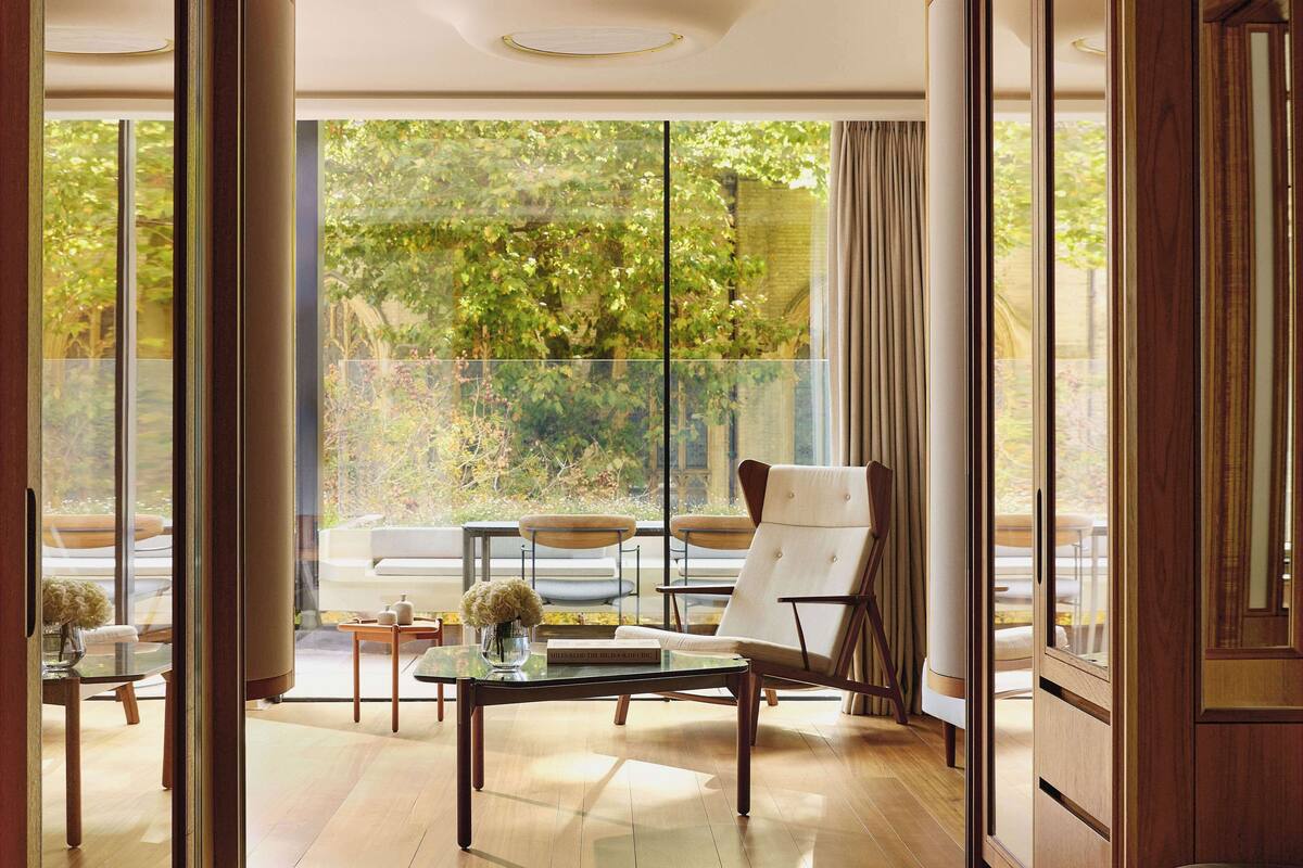 A modern interior with a glass partition, a wooden floor, a white chair, a glass table, and a view of greenery outside.