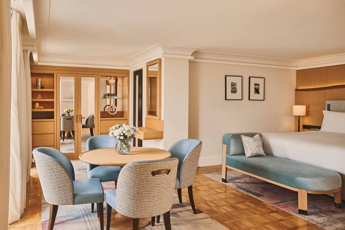 A hotel room with a bed, a sofa, a dining table with chairs, a mirror, and a wardrobe.
