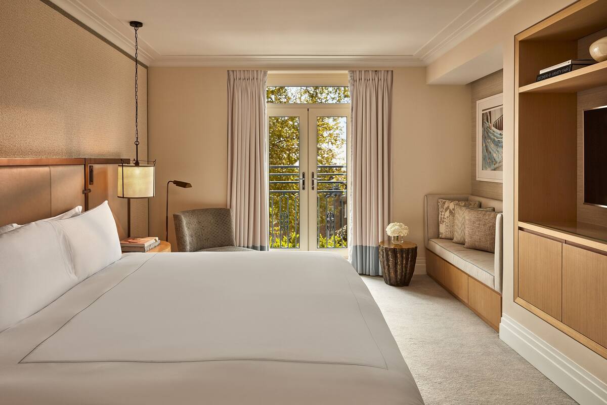 A hotel room with a large bed, a desk, a chair, a small table with a vase, a sofa, and a TV.