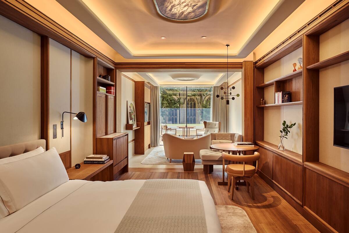 A modern hotel room with a large bed, a sitting area with a table and chairs, a television, and a view of the outdoors.