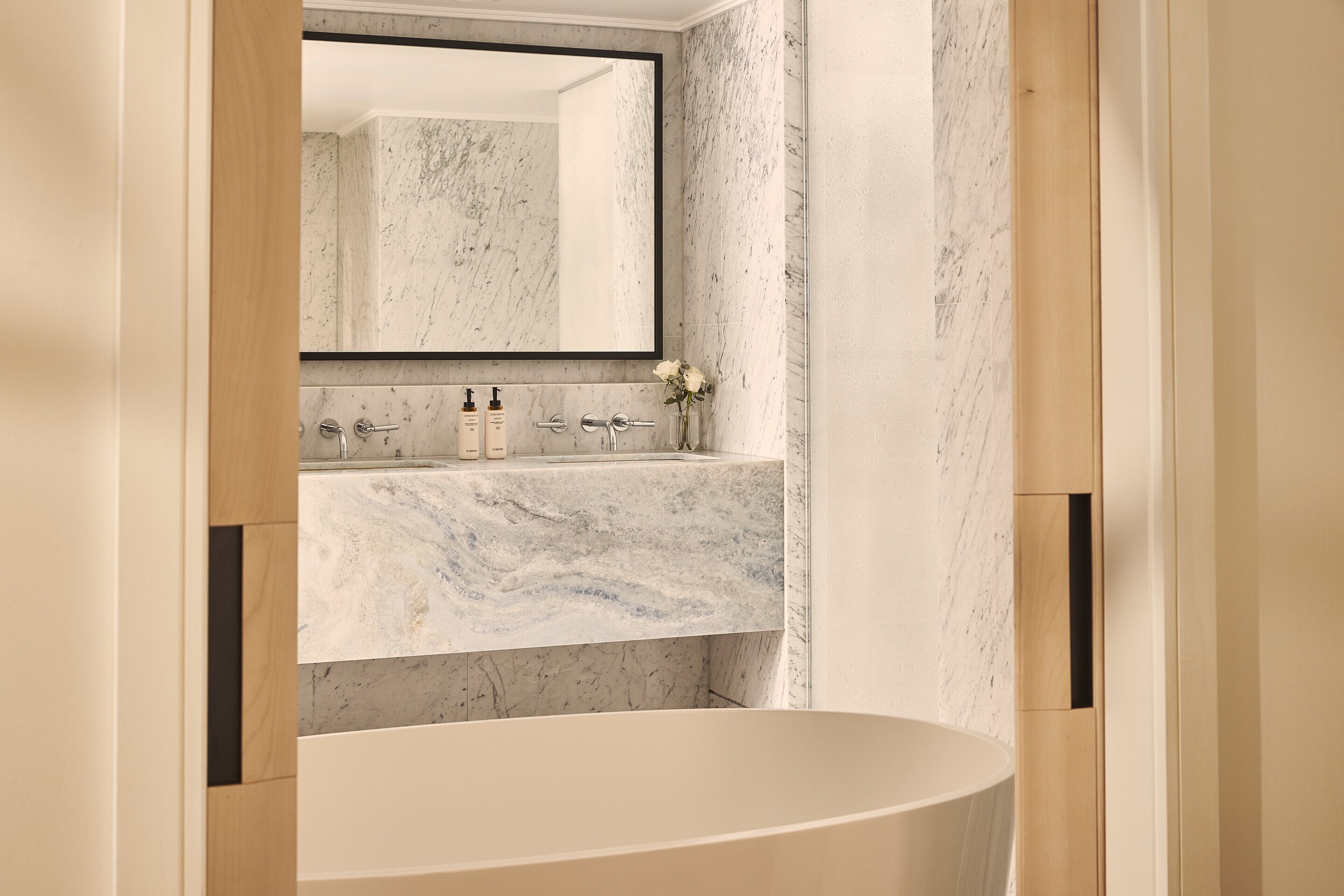 A bathroom with a marble sink, a large mirror, and a bathtub.