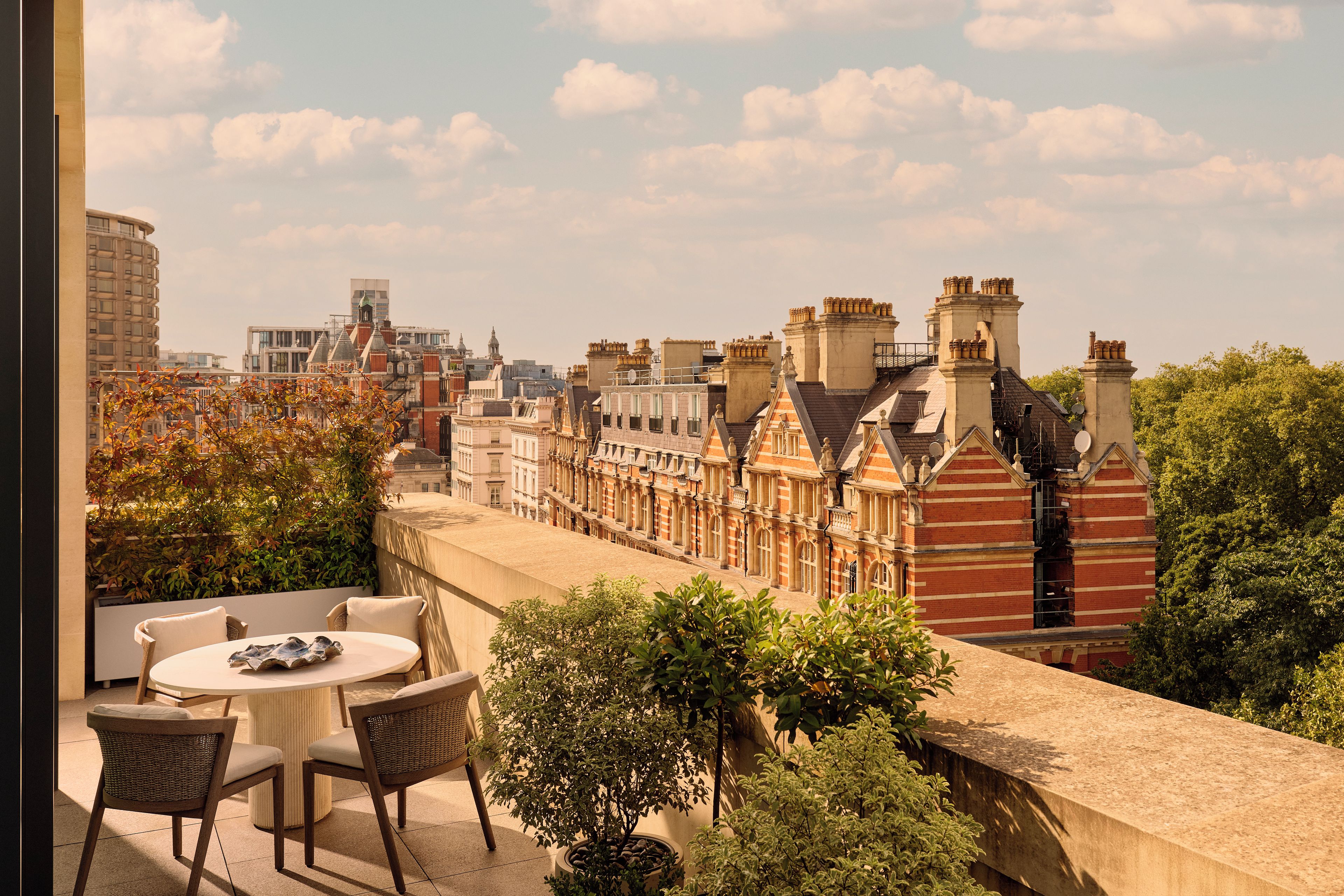 A terrace with a table and chairs, overlooking a row of traditional buildings with red brick facades and multiple chimneys.