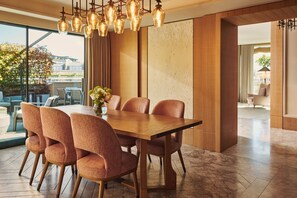 A dining area with a wooden table and six chairs, a vase with flowers, and a view of the outdoors through large windows.