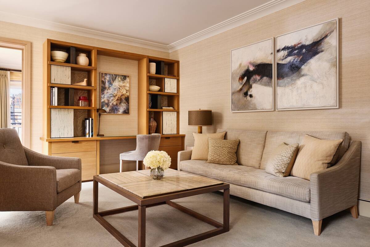 A living room with a sofa, armchair, coffee table, bookshelf, and artwork on the wall.