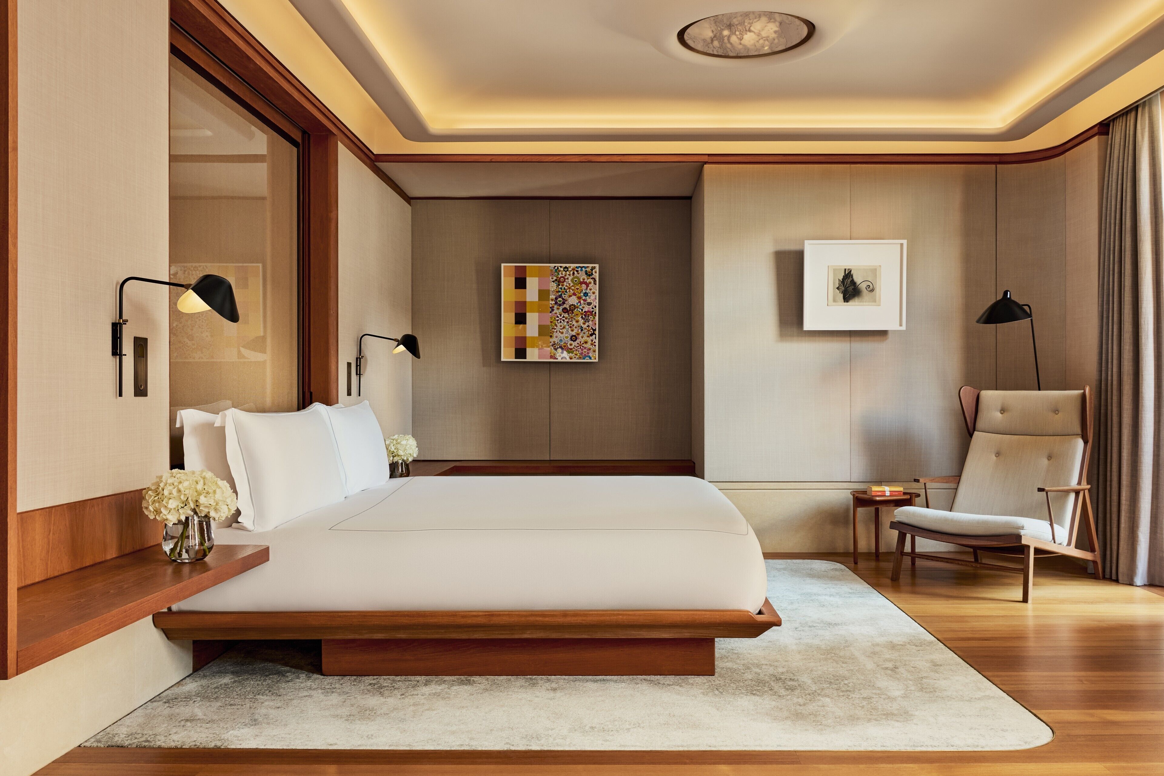 A modern bedroom with a large bed, bedside tables, a chair, and artwork on the walls.