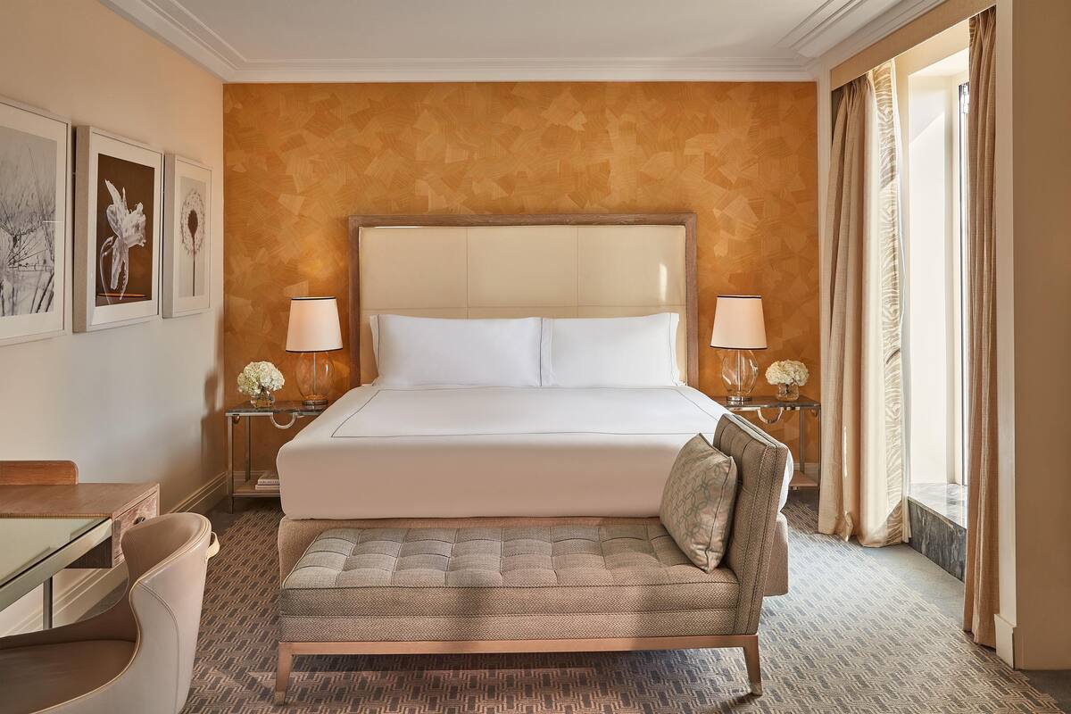 A hotel room with a large bed, two bedside lamps, a sofa, a desk, and framed artwork on the wall.