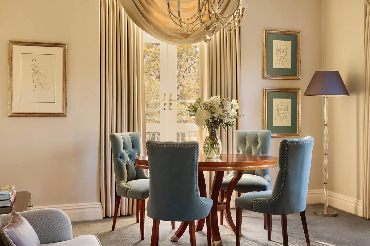 A dining area with a round wooden table surrounded by four upholstered chairs, a vase with flowers, and framed artwork on the walls.