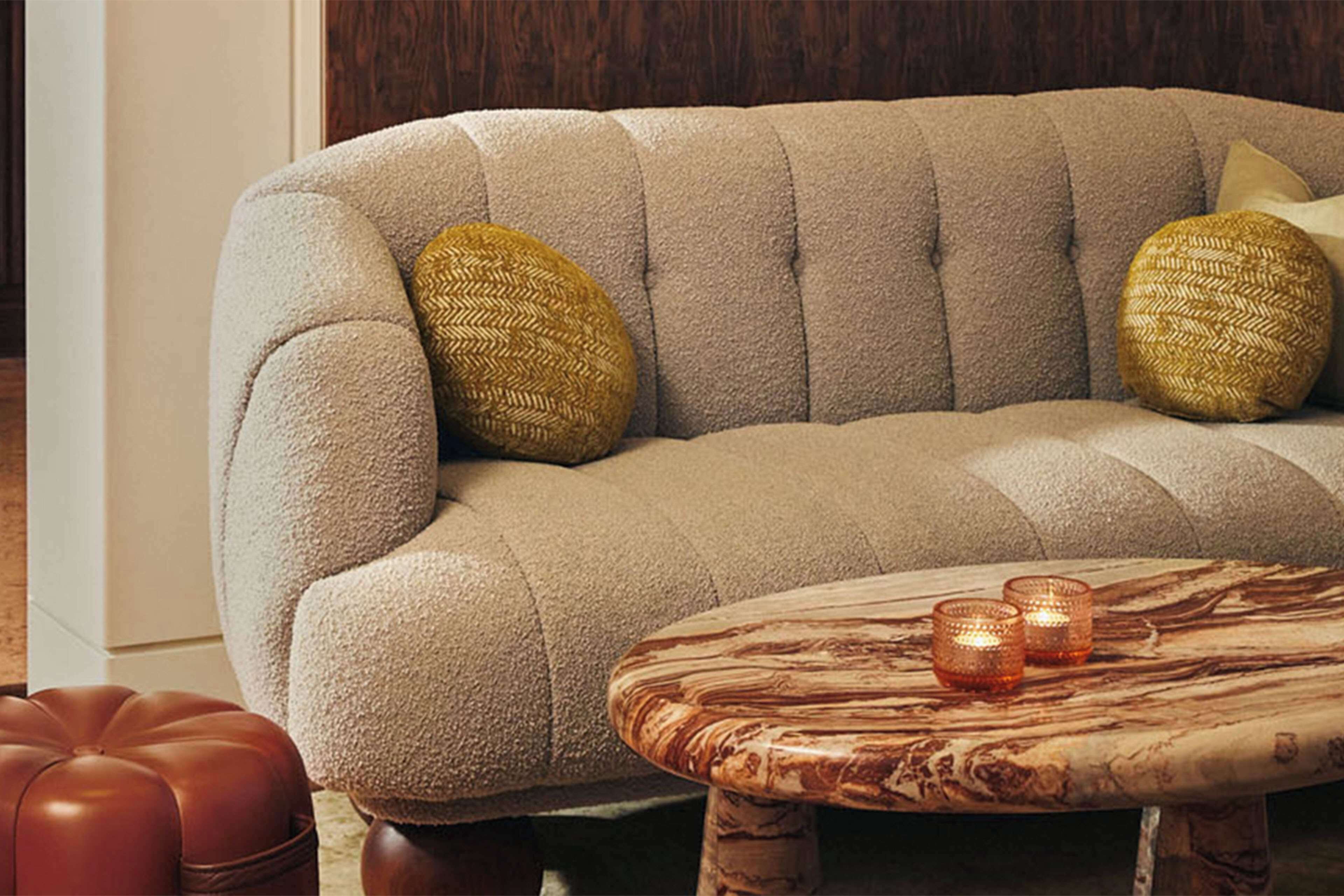 A tufted sofa with two decorative pillows, a wooden coffee table with a marble-like pattern, and a leather ottoman.