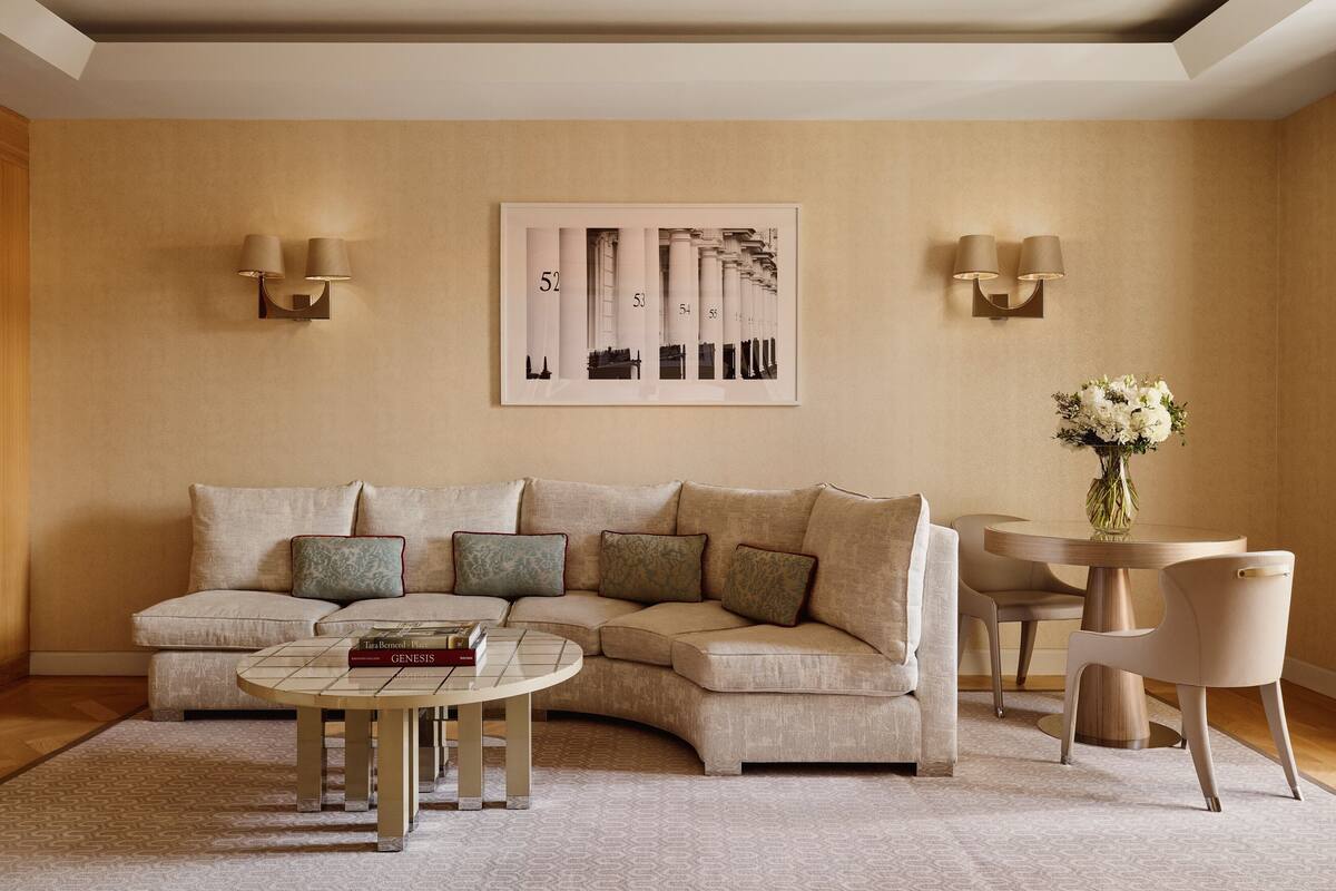 A living room with a beige sectional sofa, a coffee table, a round table with chairs, and wall-mounted lamps.