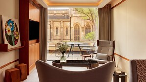 A modern hotel room with a large window, a flat-screen TV, a comfortable seating area, and a decorative painting. - The Berkeley, Maybourne  (London)