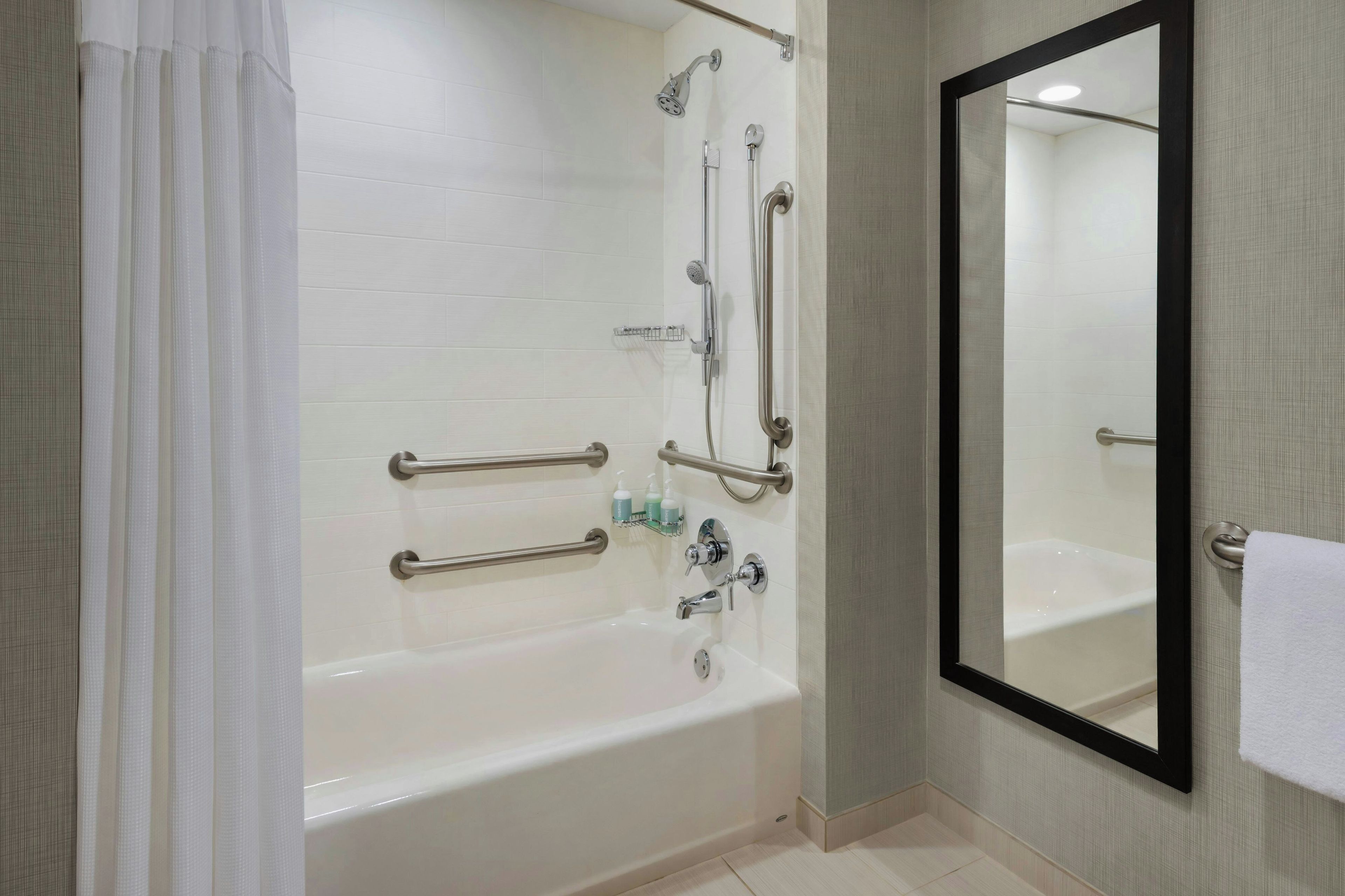 A modern bathroom with a bathtub, shower, and handrails.