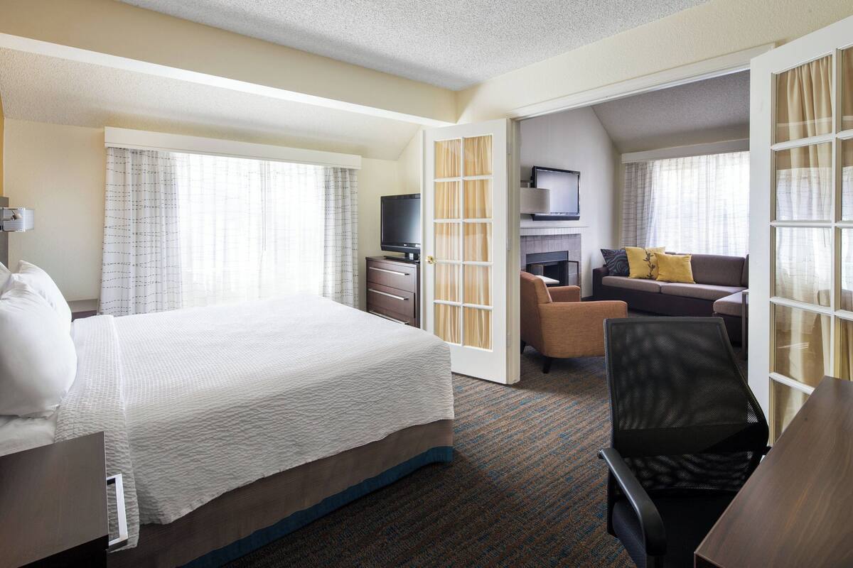 Een hotelkamer met een groot bed, een bureau, een stoel, een bank, een televisie en een open haard.