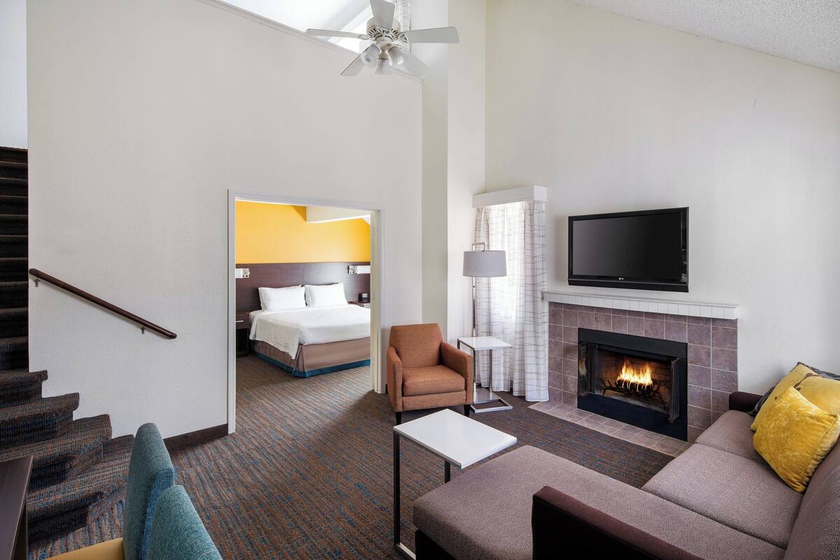 Een hotelkamer met een open haard, een televisie, een bank, een stoel en een bed.