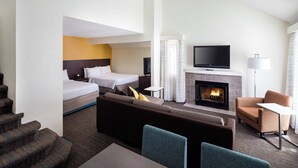 Una habitación de hotel con sofá, cama, televisión, chimenea y escalera.