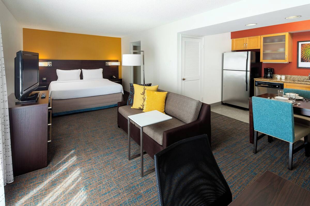 Een hotelkamer met een bed, een slaapbank, een bureau met stoel, een televisie en een koelkast.