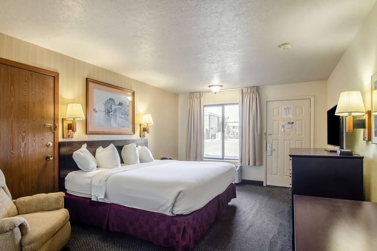 A hotel room with a large bed, a desk, a chair, and a window with curtains.