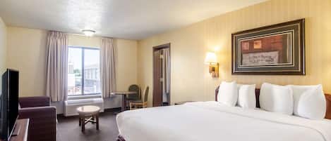 A hotel room with a large bed, a desk, a chair, a television, and a window with curtains.