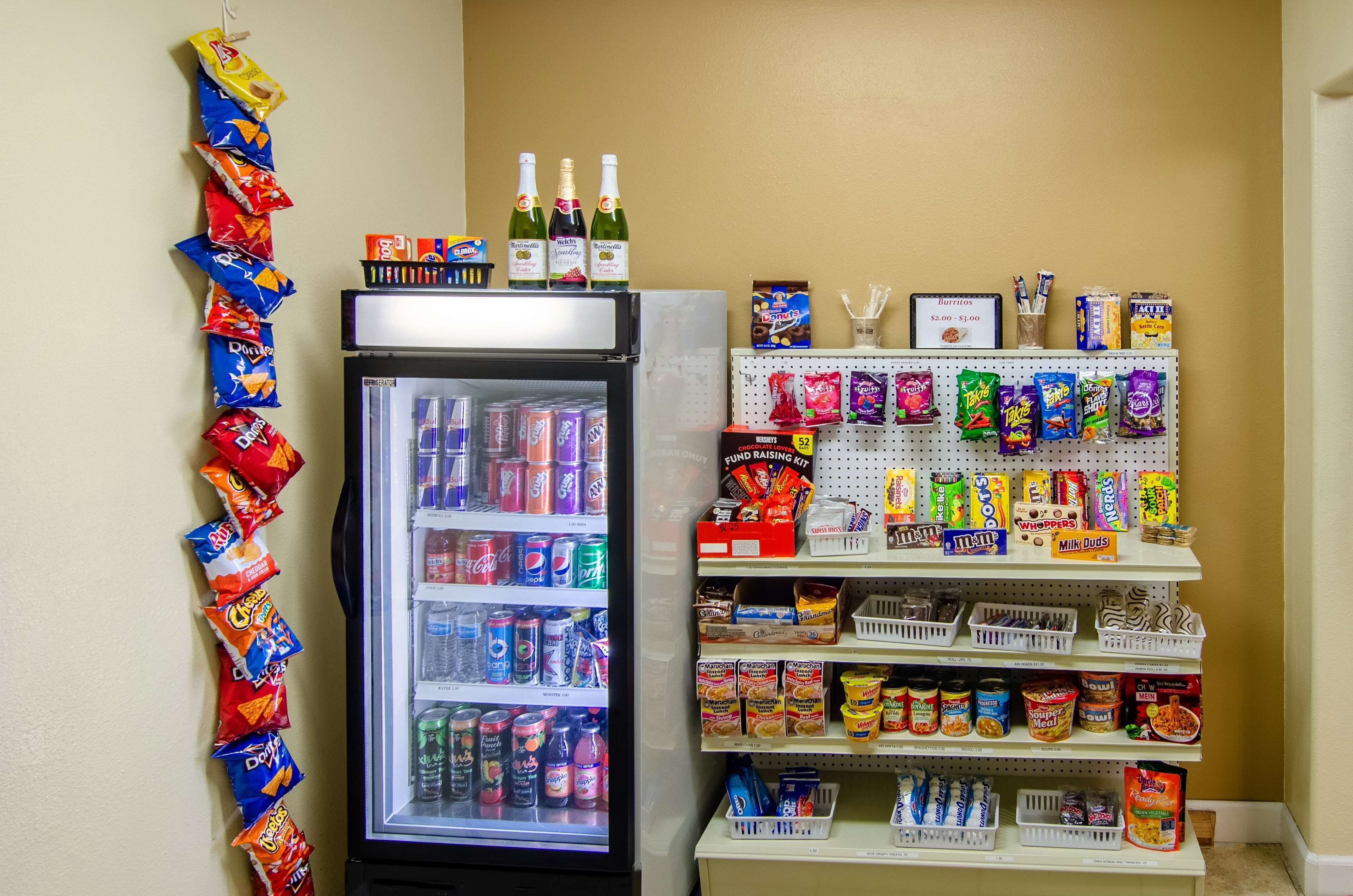 A vending machine stocked with snacks and drinks, a refrigerator with beverages, and a shelf with various packaged goods.