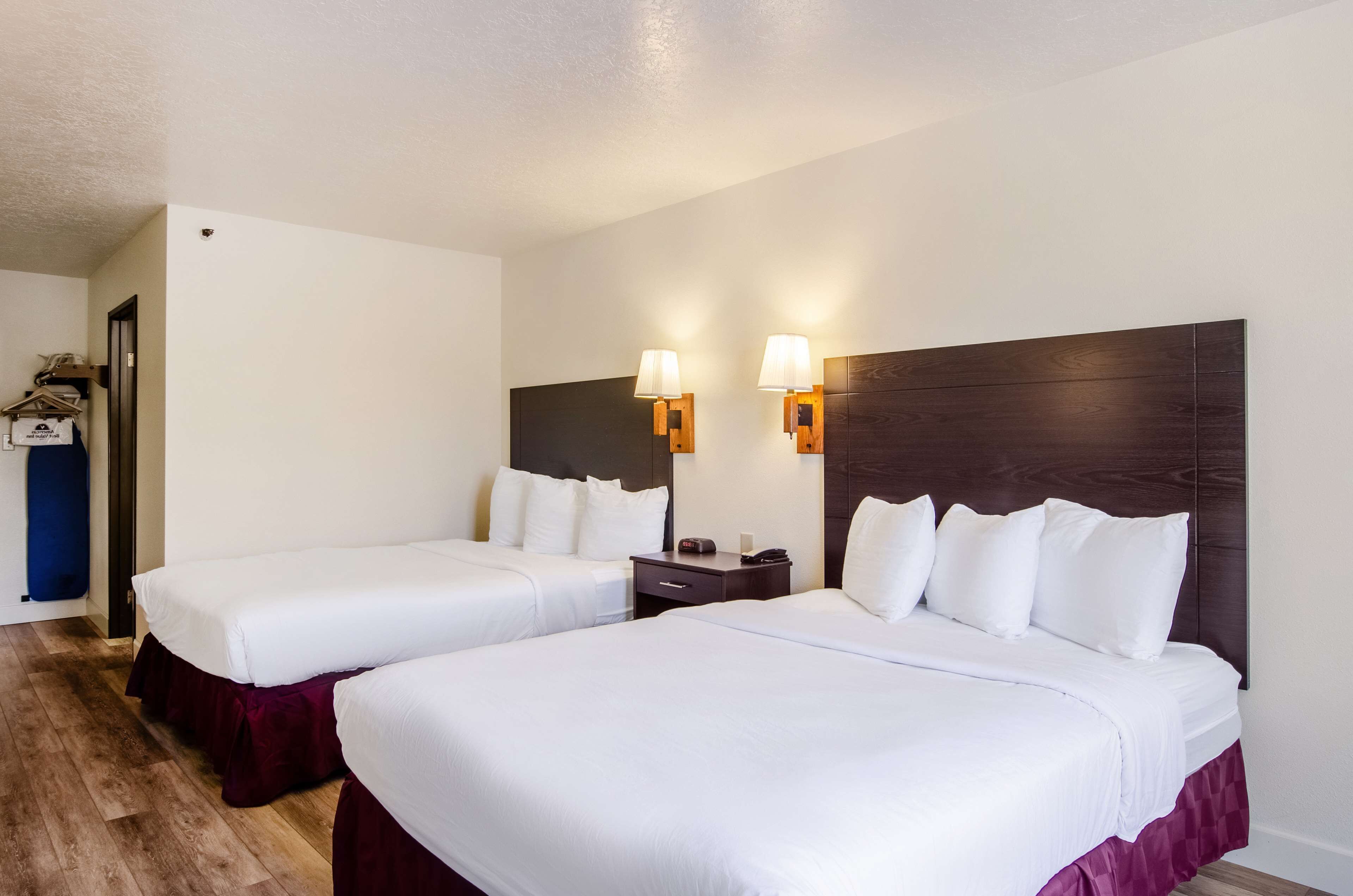 Ein Hotelzimmer mit zwei Betten, einem Holzkopfstück, Nachttischlampen und Holzboden.