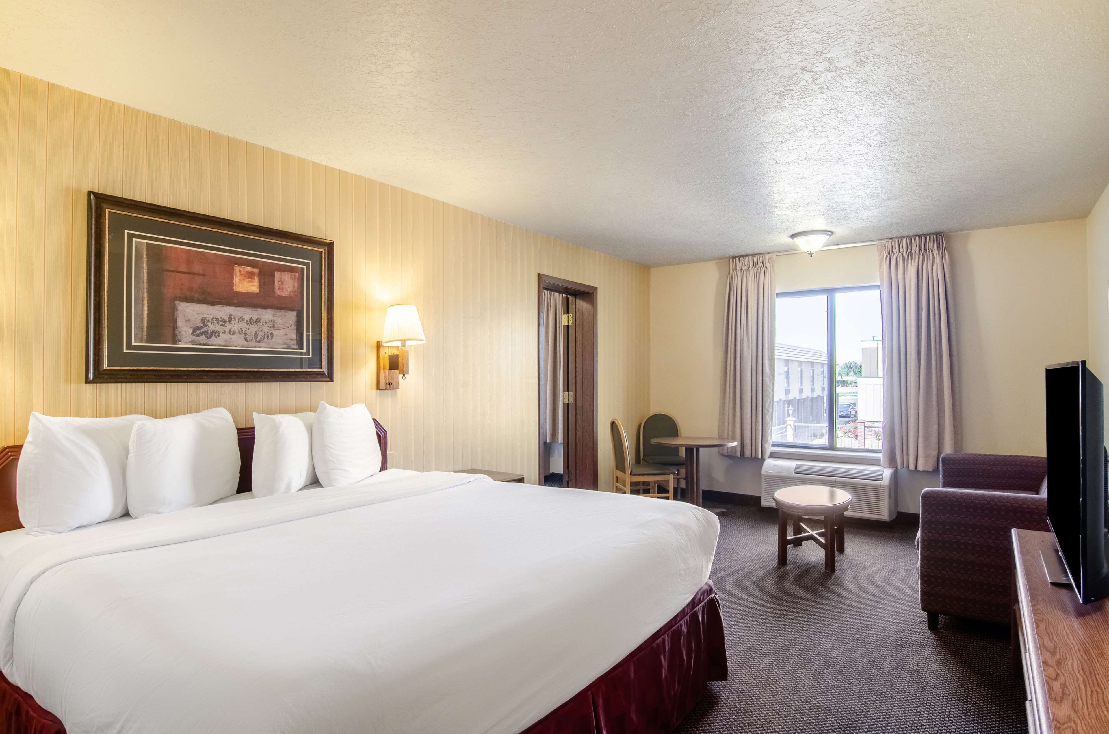 Quarto de hotel com uma cama grande, uma escrivaninha, uma cadeira, uma televisão e uma janela com cortinas.