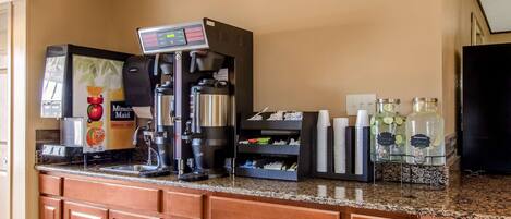 Una estación de café con una máquina de café, un dispensador de jugo de fruta y un dispensador de bebidas.